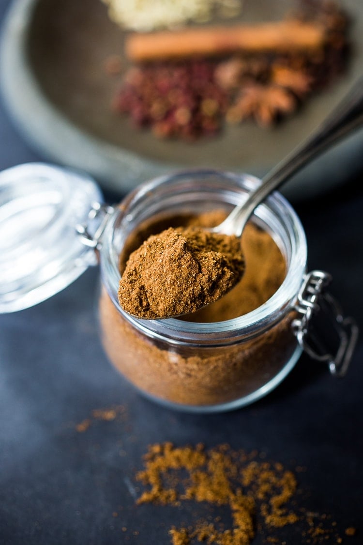 glass jar with spoon holding up scoop of homemade Chinese Five Spice.