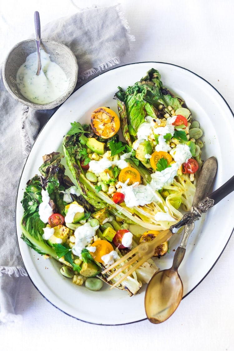 serving plate with grilled romaine salad with corn, fava beans and avocado with dressing drizzled over top.