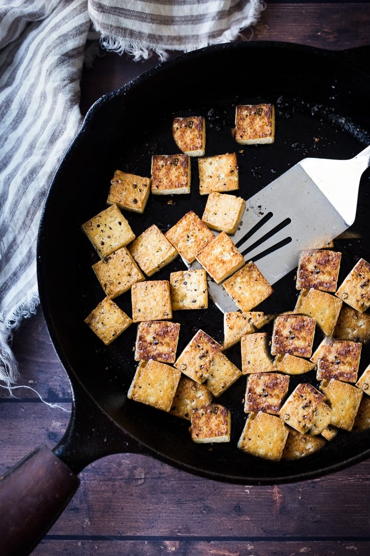 cast iron skillet with metal spatula and seasoned crispy tofu. 