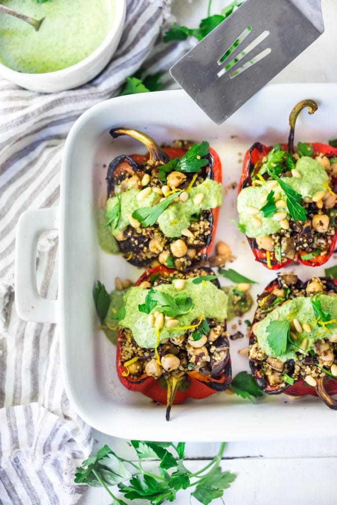 Quinoa Stuffed Peppers with eggplant and chickpeas, drizzled with zhoug yogurt sauce in a baking dish. 