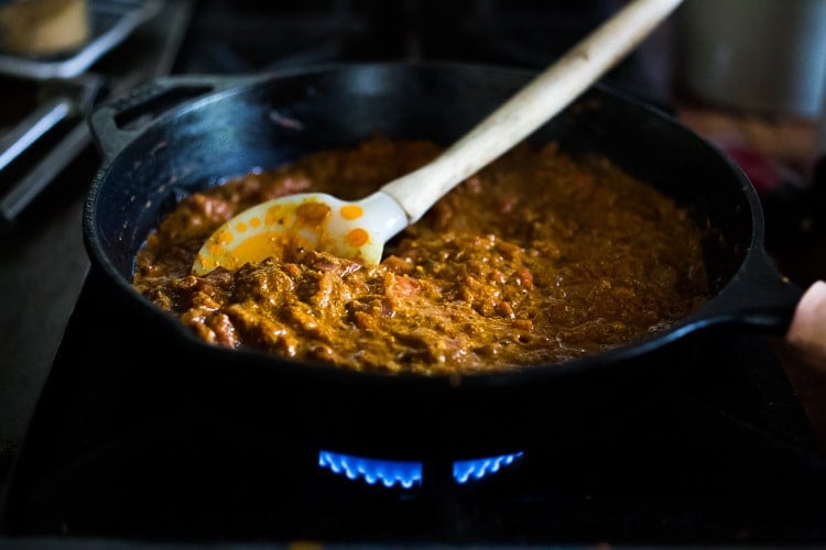 Indian curry sauce simmer on stovetop in cast iron skillet.