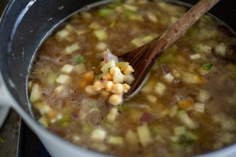 wood spoon scooping up chickpeas in lemony chickpea soup in pot. 