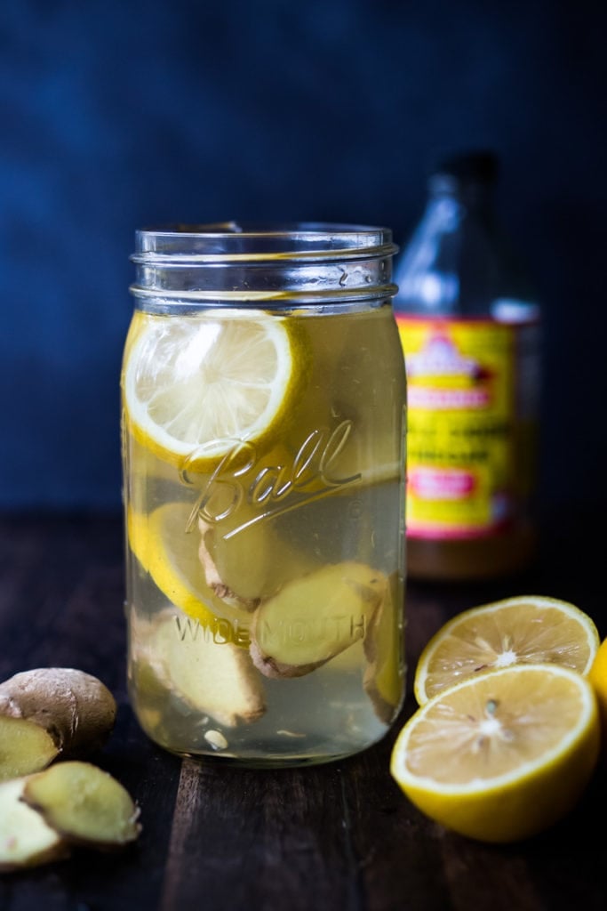 a jar filled with apple cider vinegar drink recipe with lemons, sliced ginger and mineral salt. A delicious recipe for an Apple Cider Vinegar Drink (also called a Switchel) plus 10 advantages of drinking this gut-healing, probiotic drink on a daily basis!
