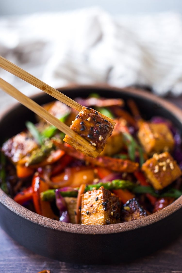 chopsticks holding a piece of tofu over bowl of szechuan tofu and veggies.