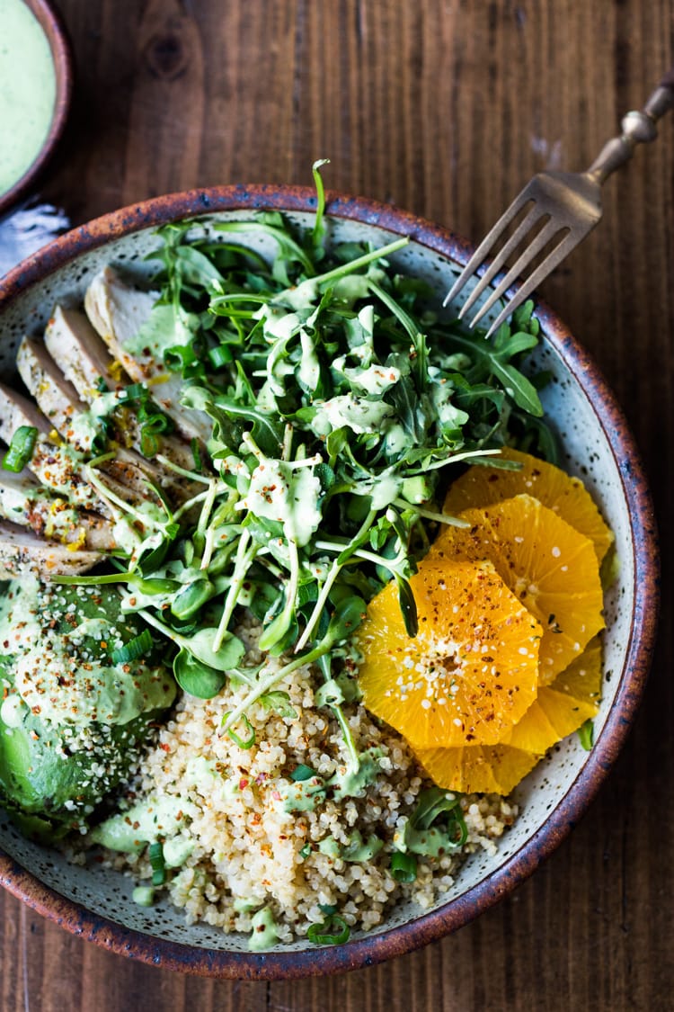 salad bowl with arugula, sprouts, chicken, orange slices, avocado, and quinoa with creamy basil dressing.
