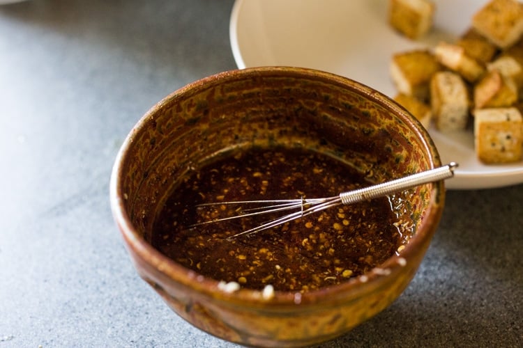 small ceramic bowl and tiny whisk with szechuan sauce.