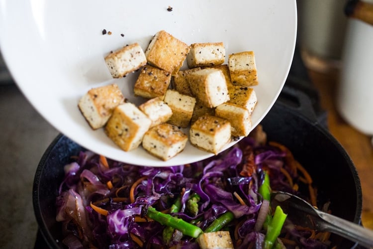 plate of crispy cubed tofu poured over top of skillet with cooked veggies.