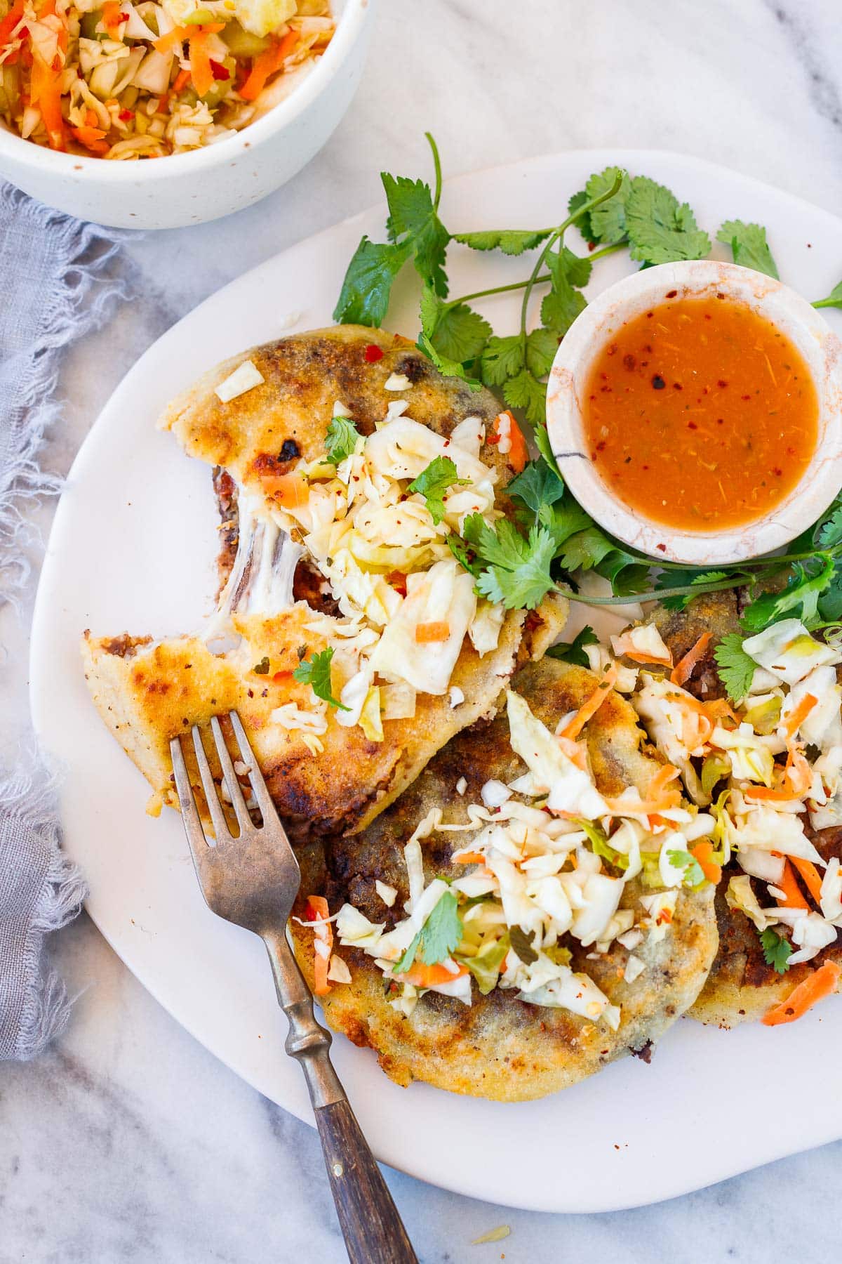 pupusas on a plate with curtido and salsa roja.