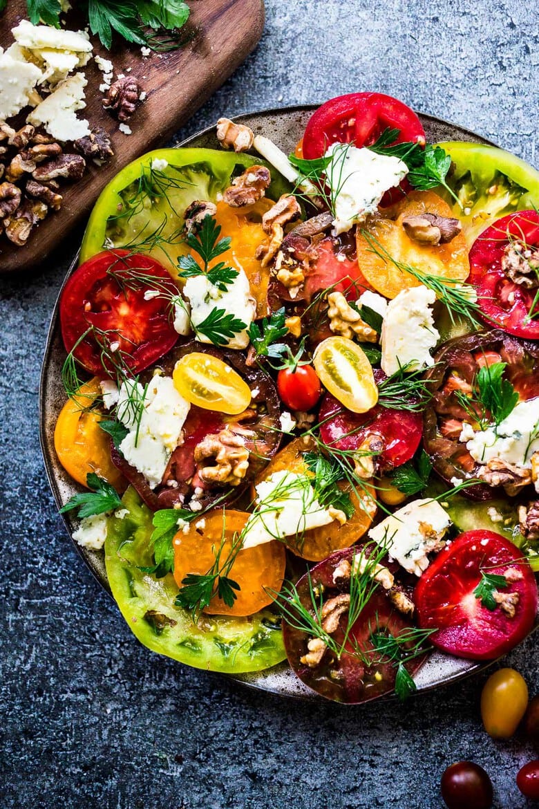 large plate with heirloom tomato salad with toasted walnuts and smoked blue cheese topped with fresh herbs.