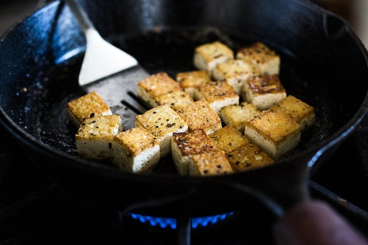 cast iron skillet with crispy tofu cooking and metal spatula. 