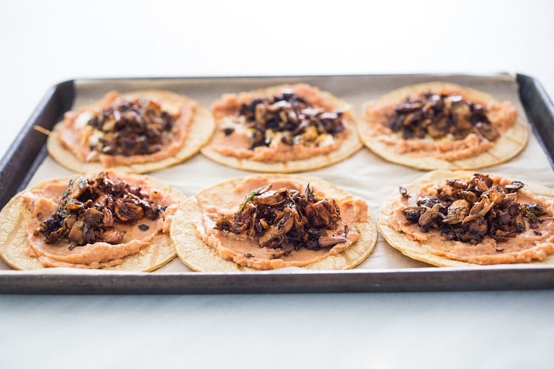six tortillas on baking sheet topped with refried beans and jackfruit carnitas.