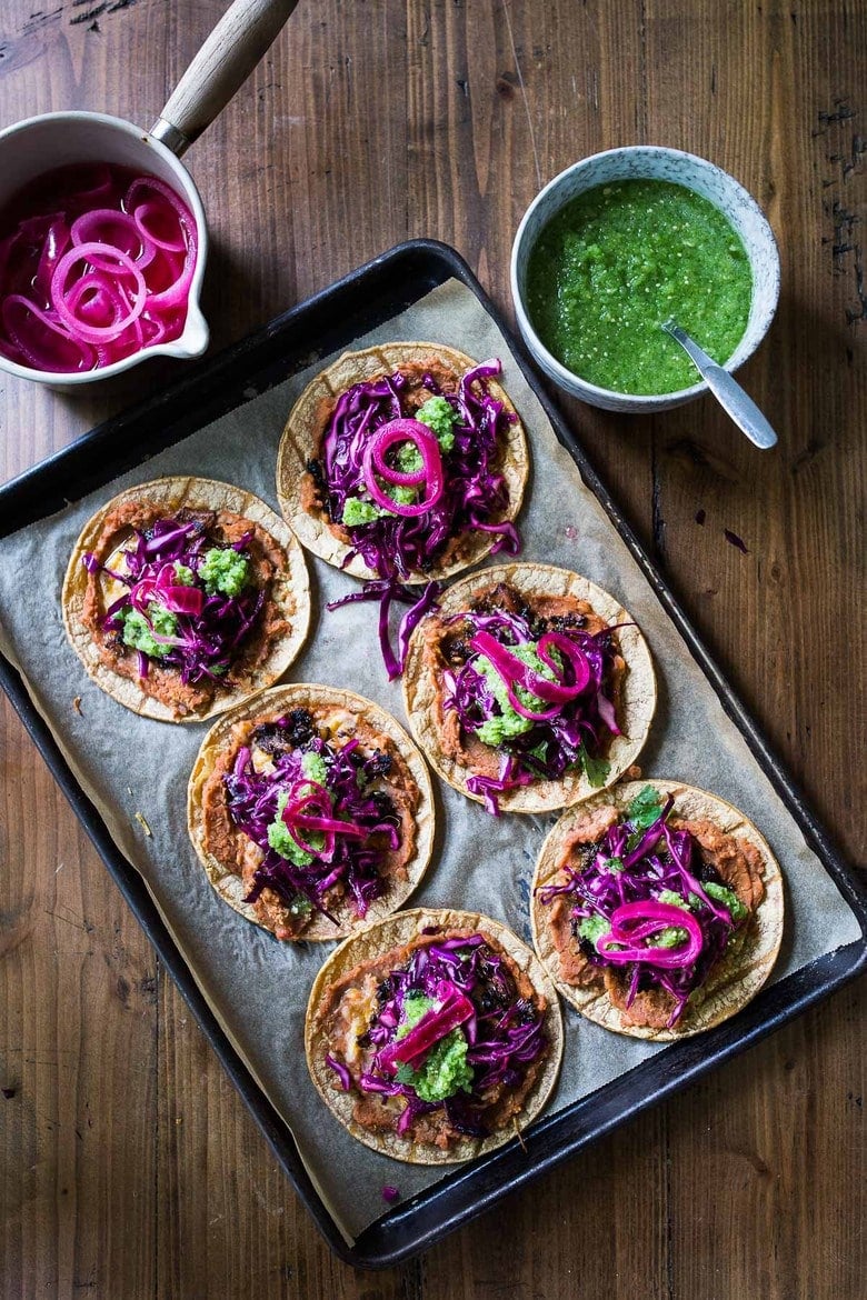 parchment-lined sheet pan with six jackfruit tacos topped with cabbage slaw, salsa, and pickled onions.