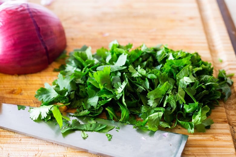 wood cutting board and sharp knife with chopped cilantro next to red onion.