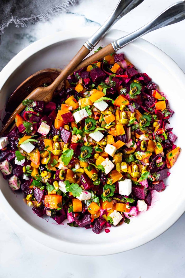 salad bowl and utensils with beet salad with feta, pistachios, and cilantro.