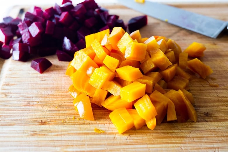 wood cutting board with sharp knife with cubed red and golden beets.