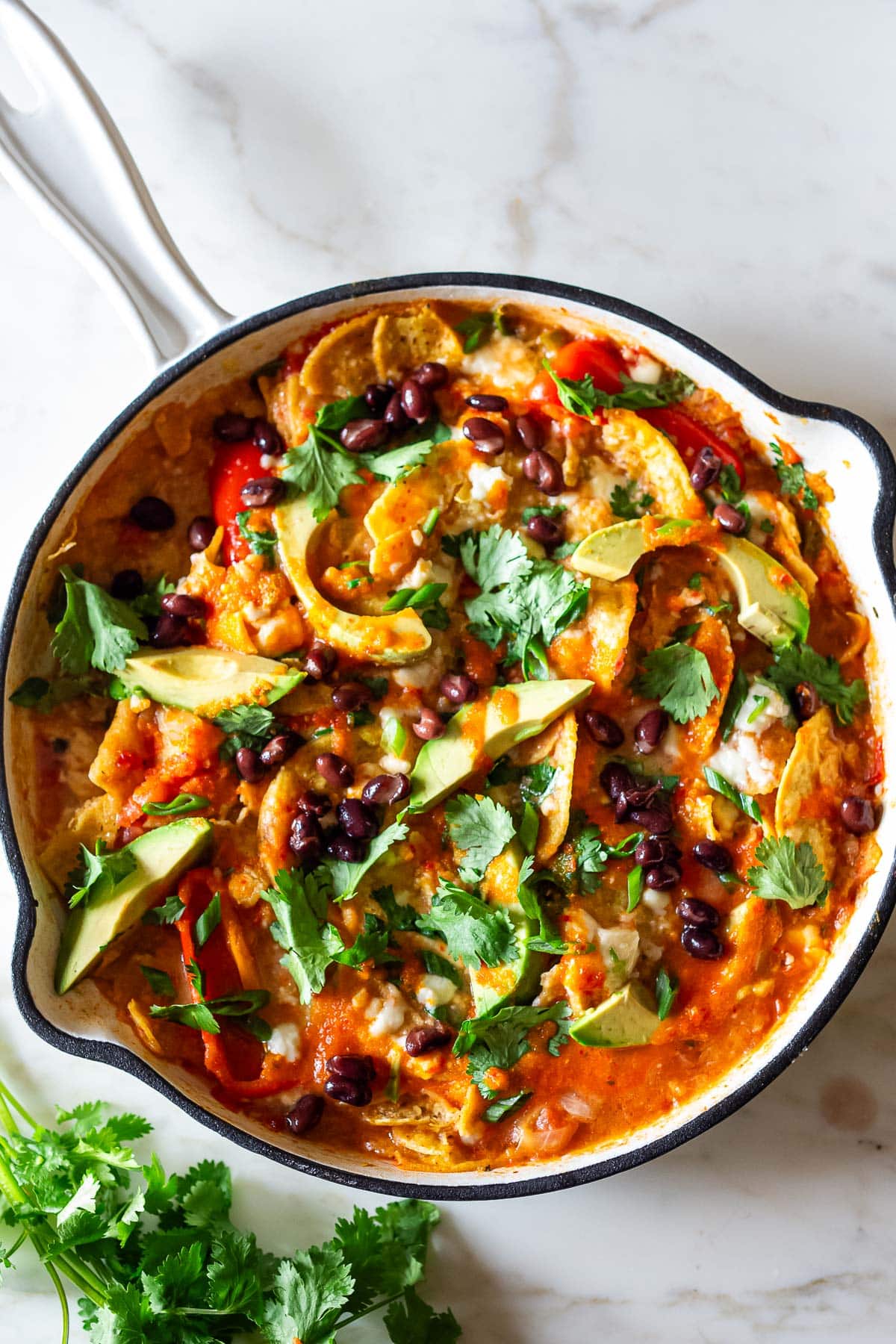 Chilaquiles in a skillet with avocado, cilantro and blackbeans. 