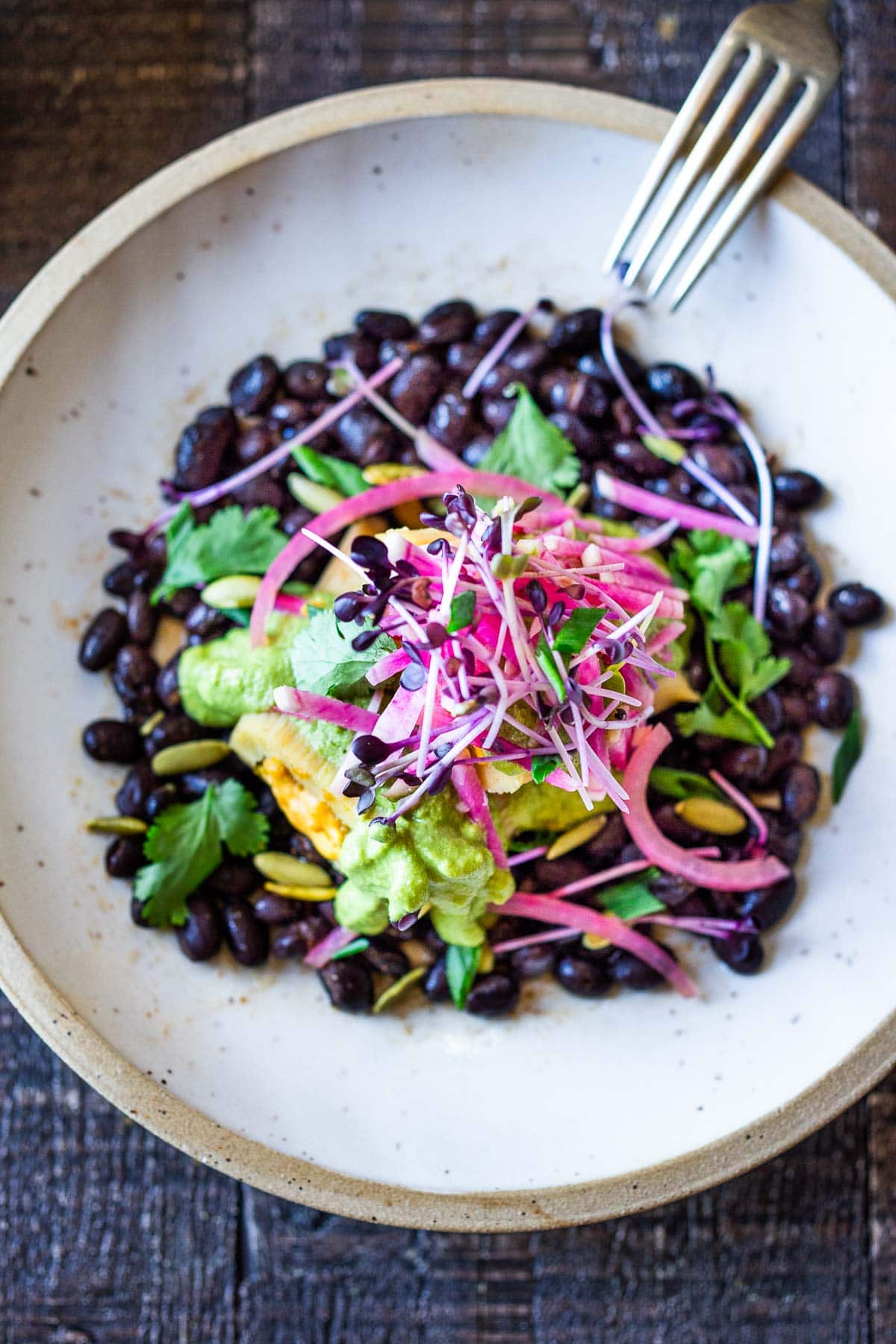 Vegetarian tamales topped with a flavorful poblano sauce and served over a bed of seasoned black beans, with microgreens, and pickled red onions.