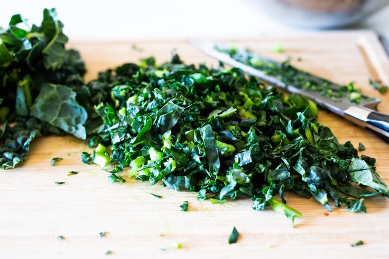 wood cutting board with sharp knife chopping lacinato kale.