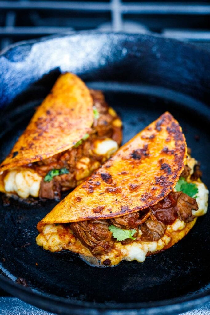 birria tacos with queso, frying in skillet.