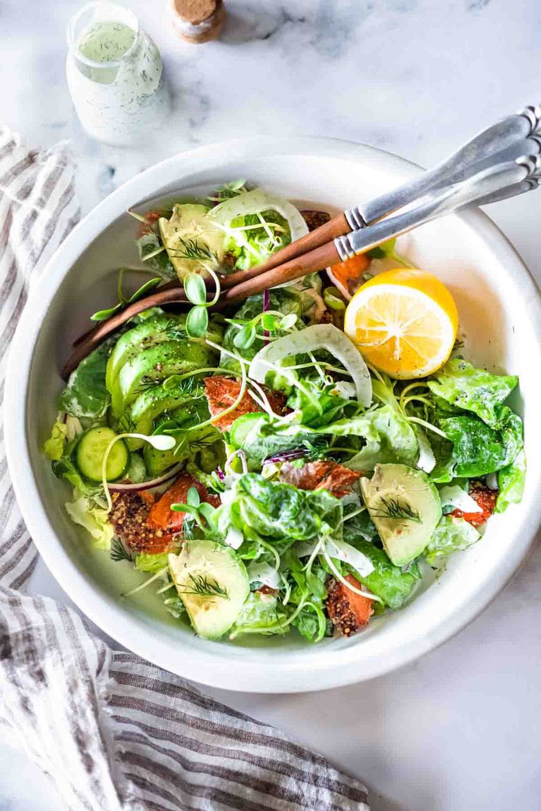 salad bowl and utensils with smoked salmon, avocado and fennel salad served with creamy dill dressing and a lemon halve.