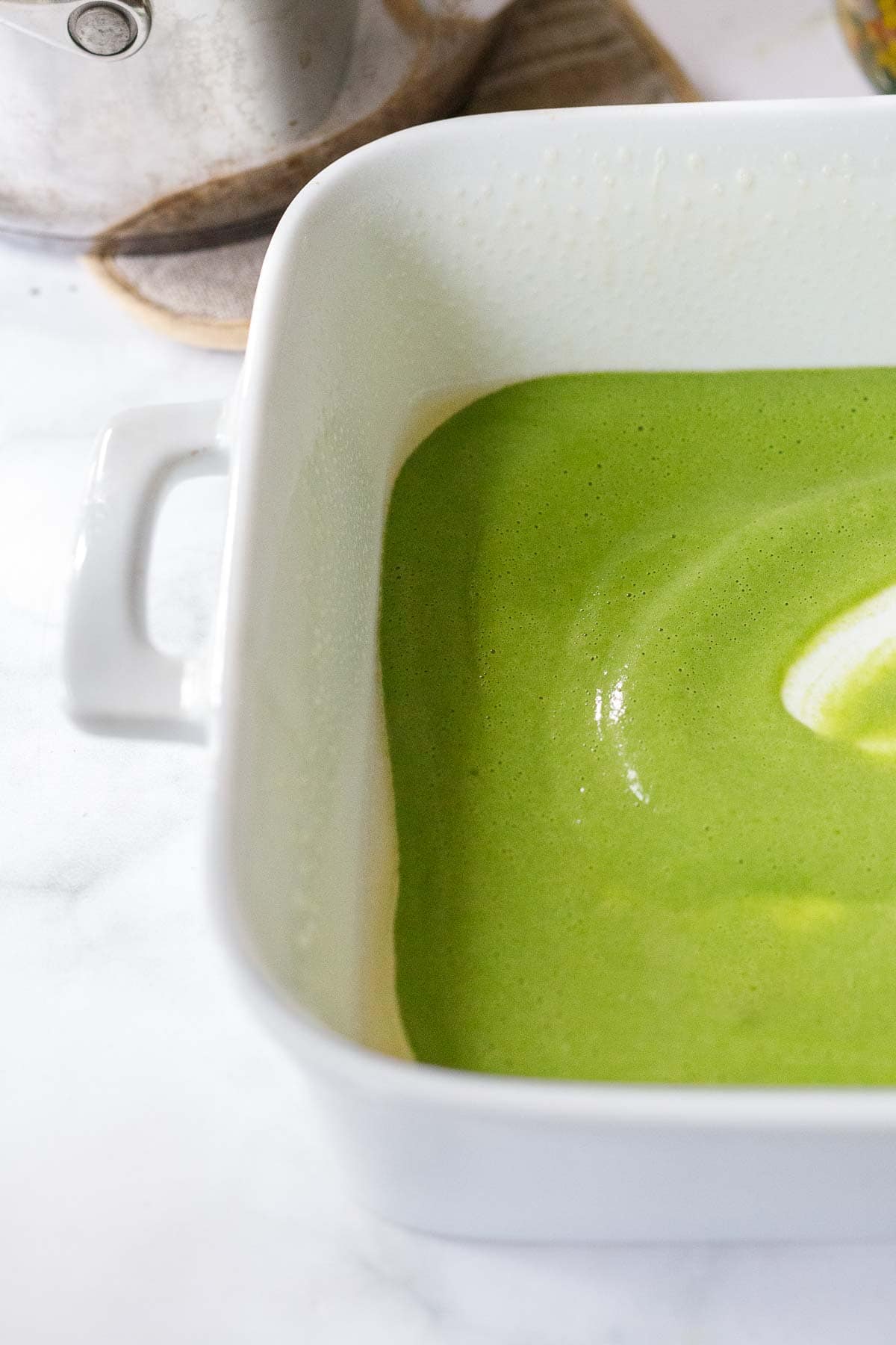Spreading Spinach basil sauce on a greased baking pan.