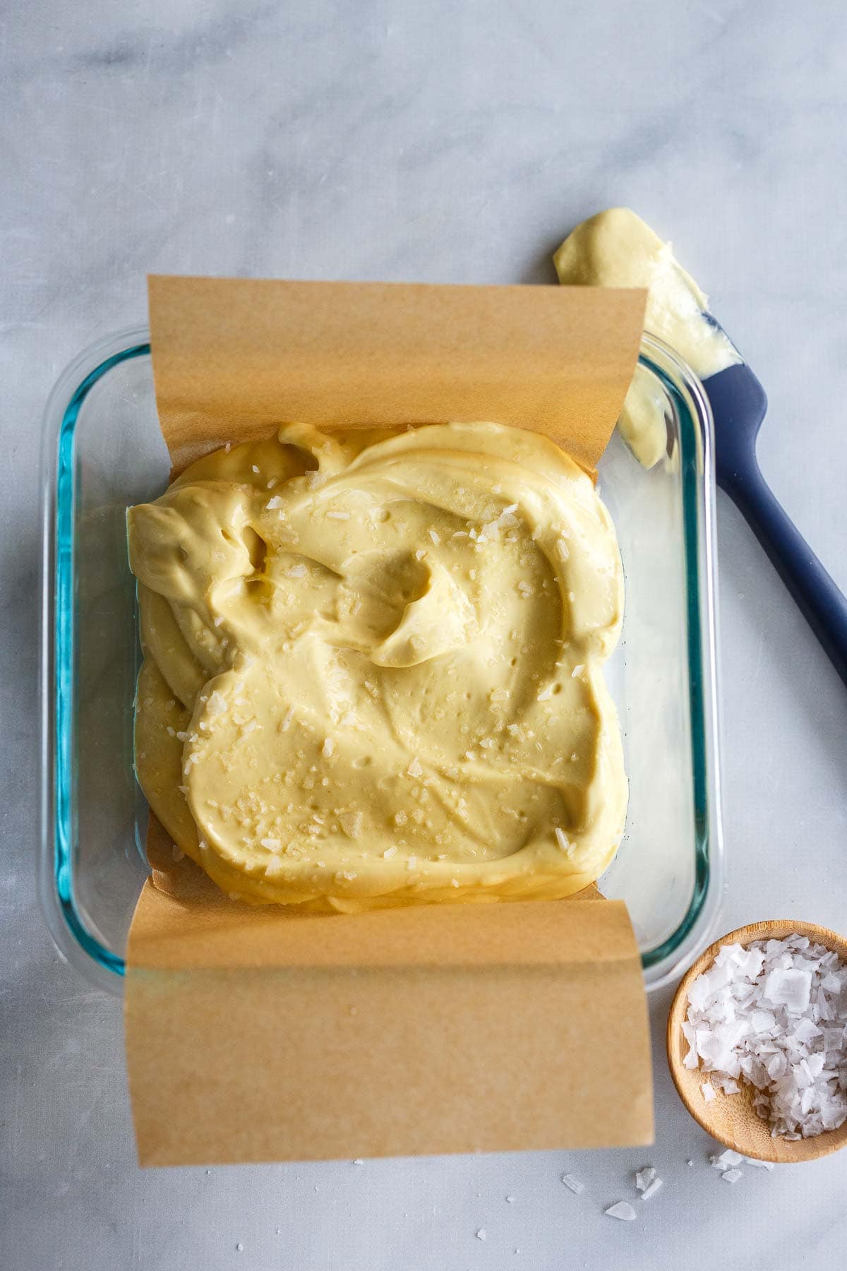 blended vegan parmesan with smooth and creamy texture in glass dish with parchment paper and coarse salt sprinkled over top.