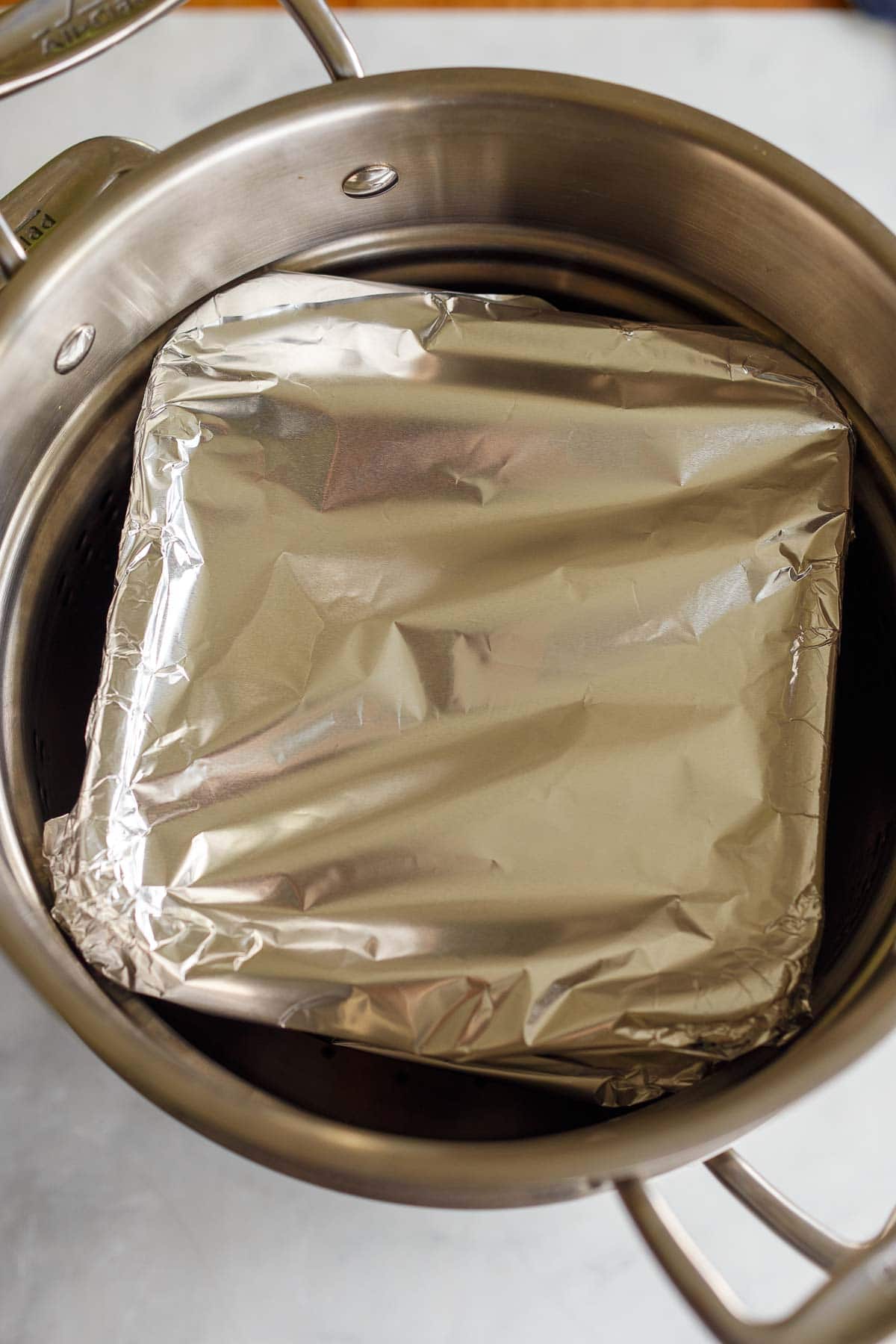 glass container wrapped in foil in steamer pot.
