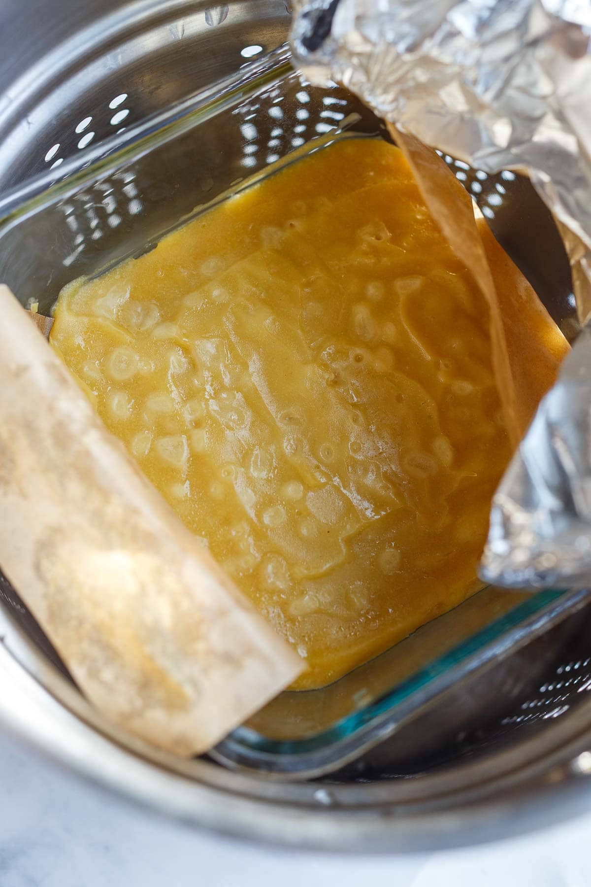 vegan parmesan in glass container with foiled pulled back to reveal its texture with after steaming.