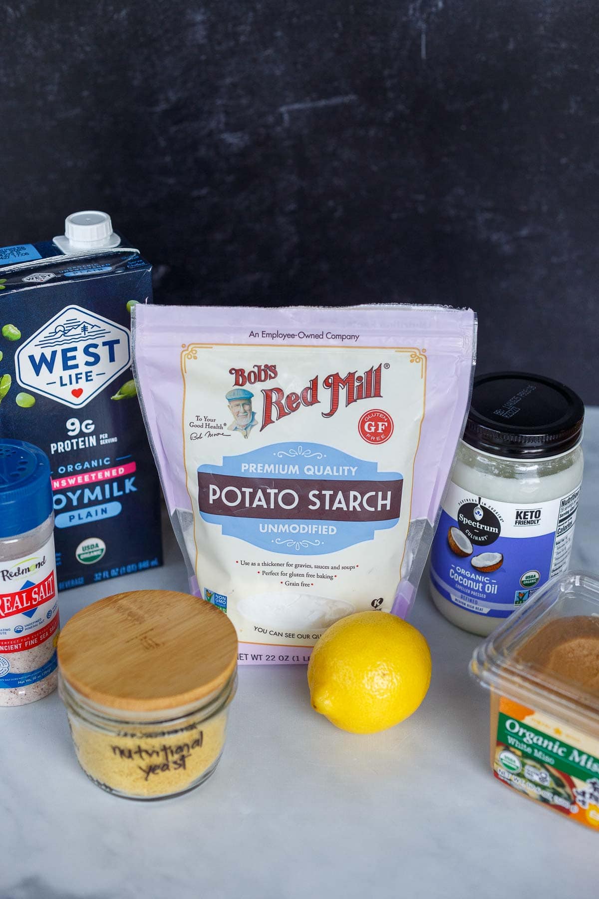 ingredients for vegan parmesan laid out - soy milk, potato starch, coconut oil, salt, nutritional yeast, lemon juice, white miso.