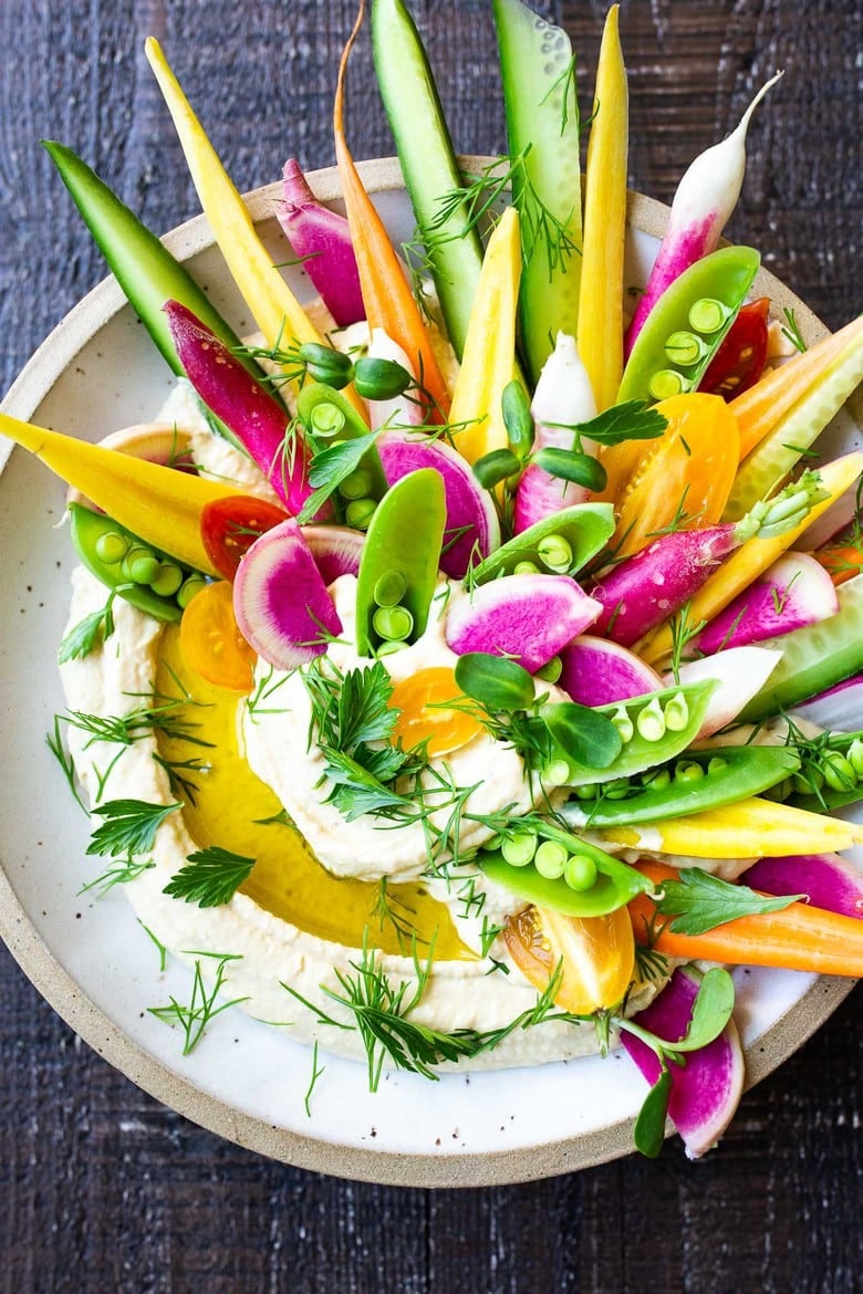 Creamy hummus with olive oil drizzle, fresh herbs, and veggies tucked in.