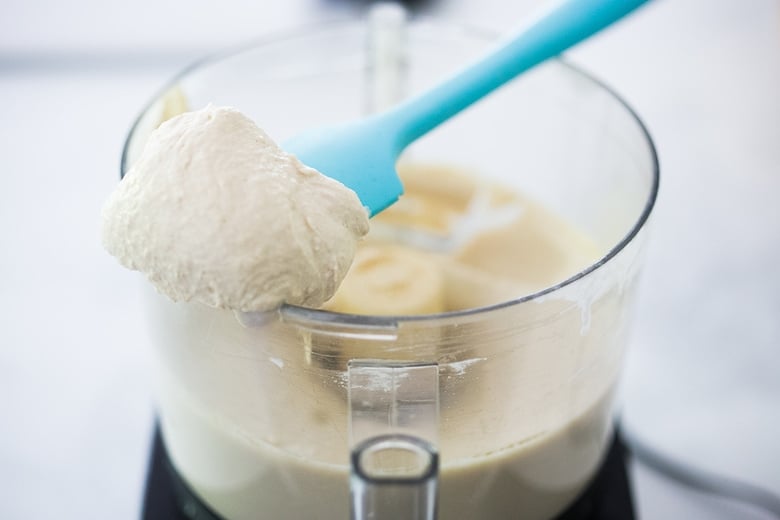 spatula scooping out homemade hummus from food processor to display ultra creamy texture.