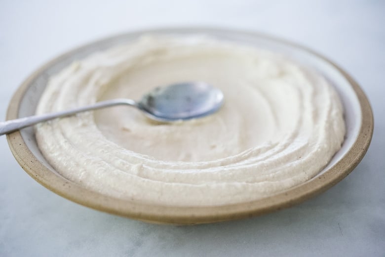 using spoon to spread hummus onto plate, creating well to pour olive oil into.