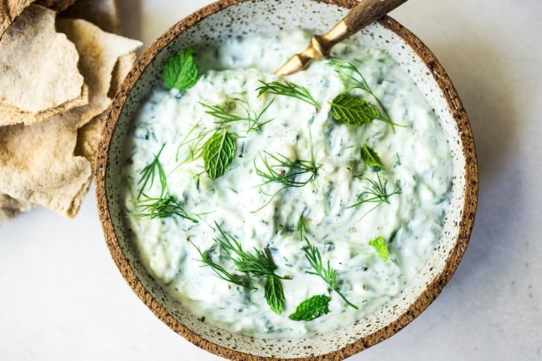 homemade tzatziki sauce in bowl with spoon, topped with fresh mint and dill. 