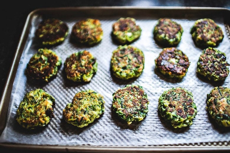 zucchini fritters staying warm on parchment lined baking sheet in oven. 