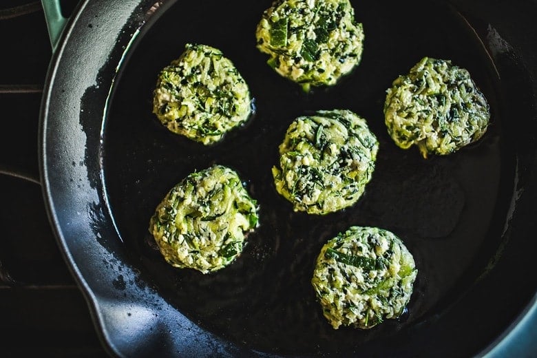 zucchini fritters searing on large cast iron skillet. 