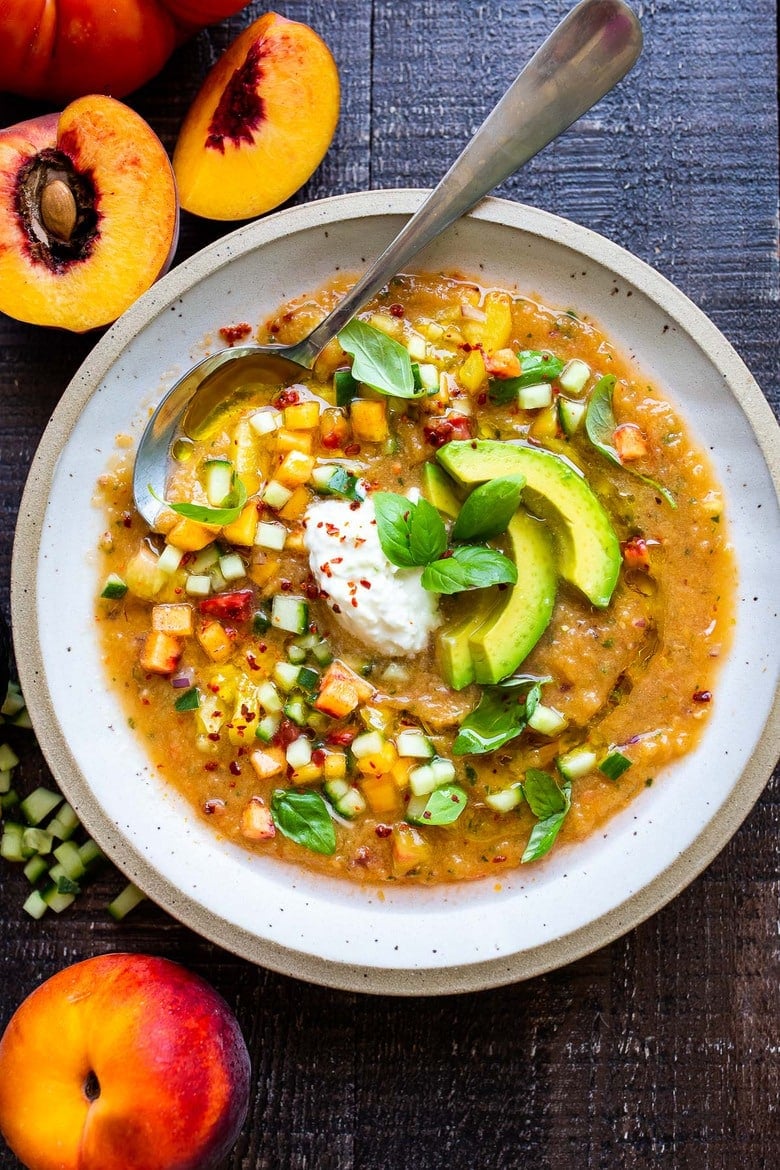 Tomato Peach Gazpacho with basil and burrata and sliced avocado in bowl with spoon.