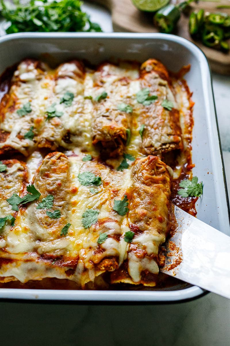 baking dish with chicken enchiladas topped with enchilada sauce and melted cheese, garnished with cilantro.