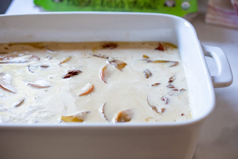 pancake batter poured into casserole dish with apples and pecans. 