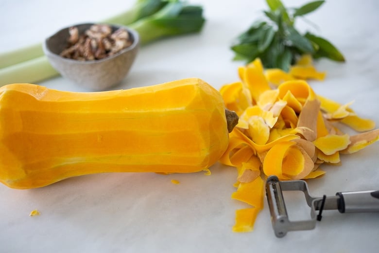 vegetable peeler and scraps next to peeled butternut squash. 