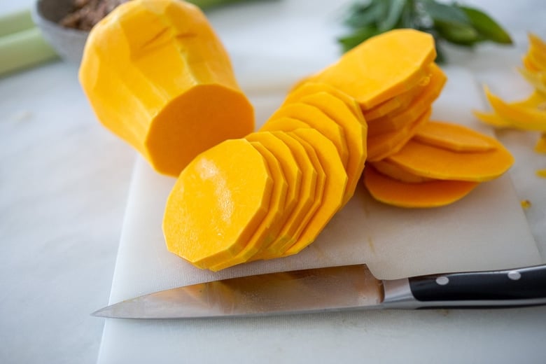 butternut squash slices on cutting board with sharp knife. 