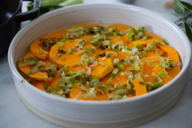 round baking dish with layer of butternut squash slices and sauteed leeks. 