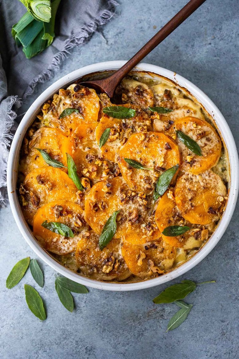 round baking dish with butternut squash gratin topped with toasted walnuts and crispy sage. 