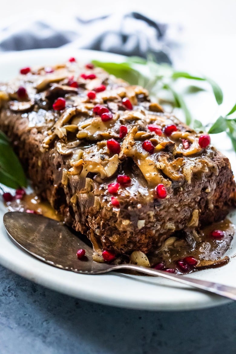 sagey walnut mushroom loaf on serving plate topped with mushroom gravy and pomegranate seeds. 