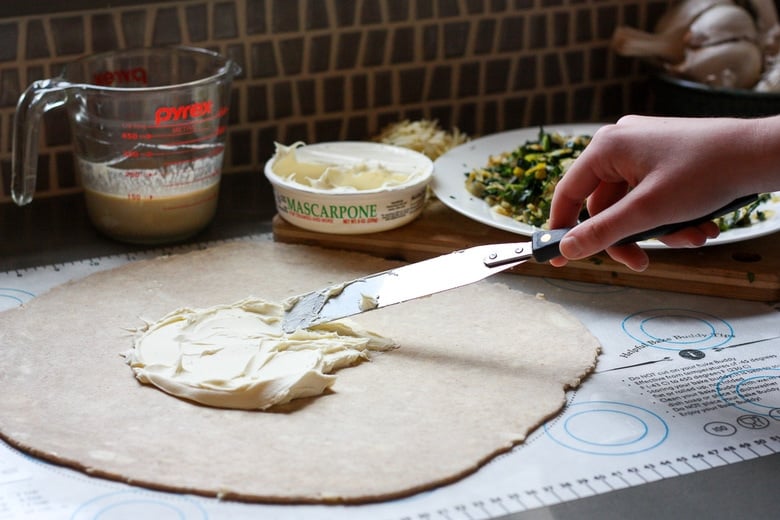 using knife to spread mascarpone cheese on galette dough.