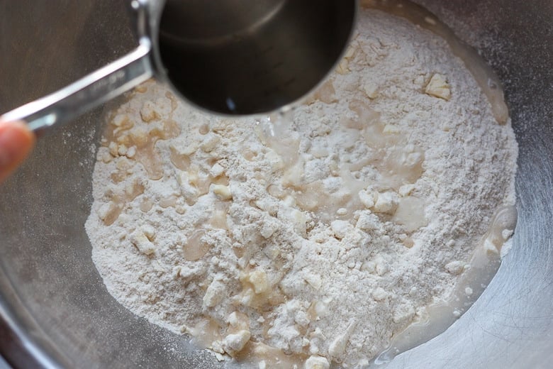 galette dough savory flour butter mixture in mixing bowl with vinegar and ice water added.