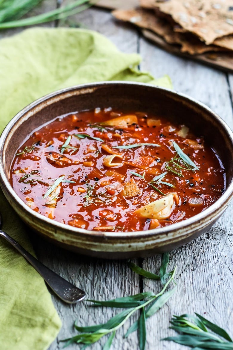 tomato artichoke soup with fennel and tarragon, garnished with herbs.