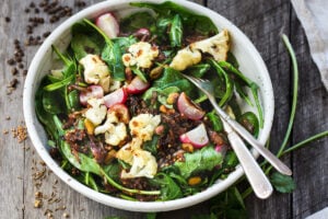 A fresh and flavorful Indian Spinach Salad with black lentils, roasted cauliflower and roasted radishes. Caramelized shallots and a Tempered Seed Dressing give the salad amazing flavor, depth and crunchy texture. #spinachsalad #indiansalad #vegan