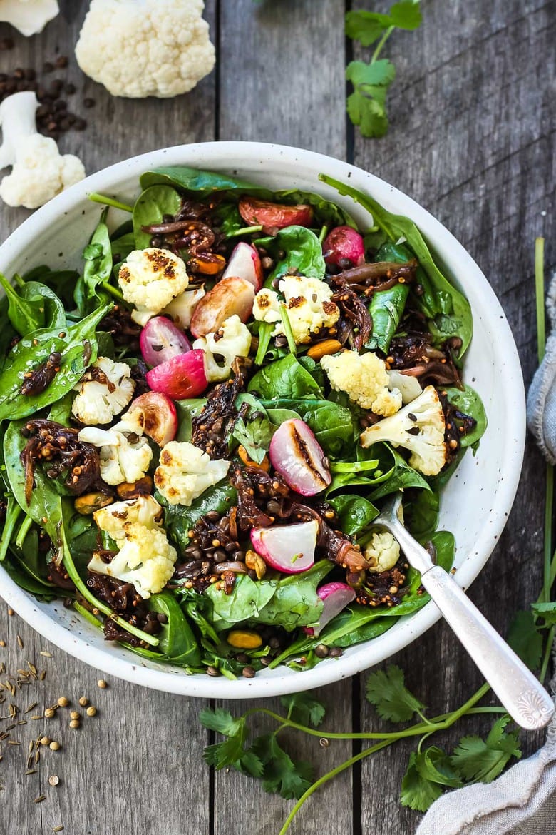 A fresh and flavorful Indian Spinach Salad with black lentils, roasted cauliflower and roasted radishes. Caramelized shallots and a Tempered Seed Dressing give the salad amazing flavor, depth and crunchy texture. #spinachsalad #indiansalad #vegan