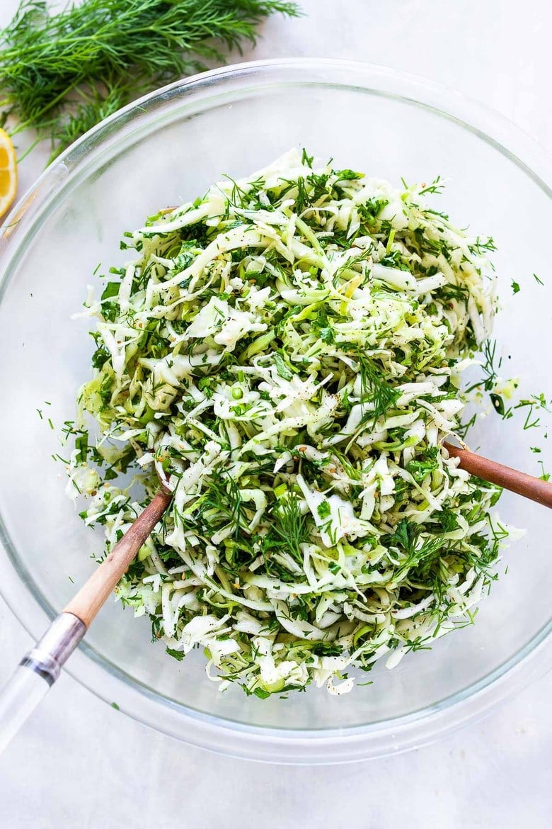 Simple Lebanese Slaw in glass mixing bowl with wood utensils.