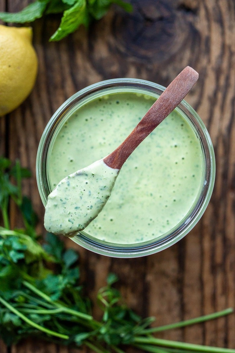 green tahini sauce in jar with spoon on top.